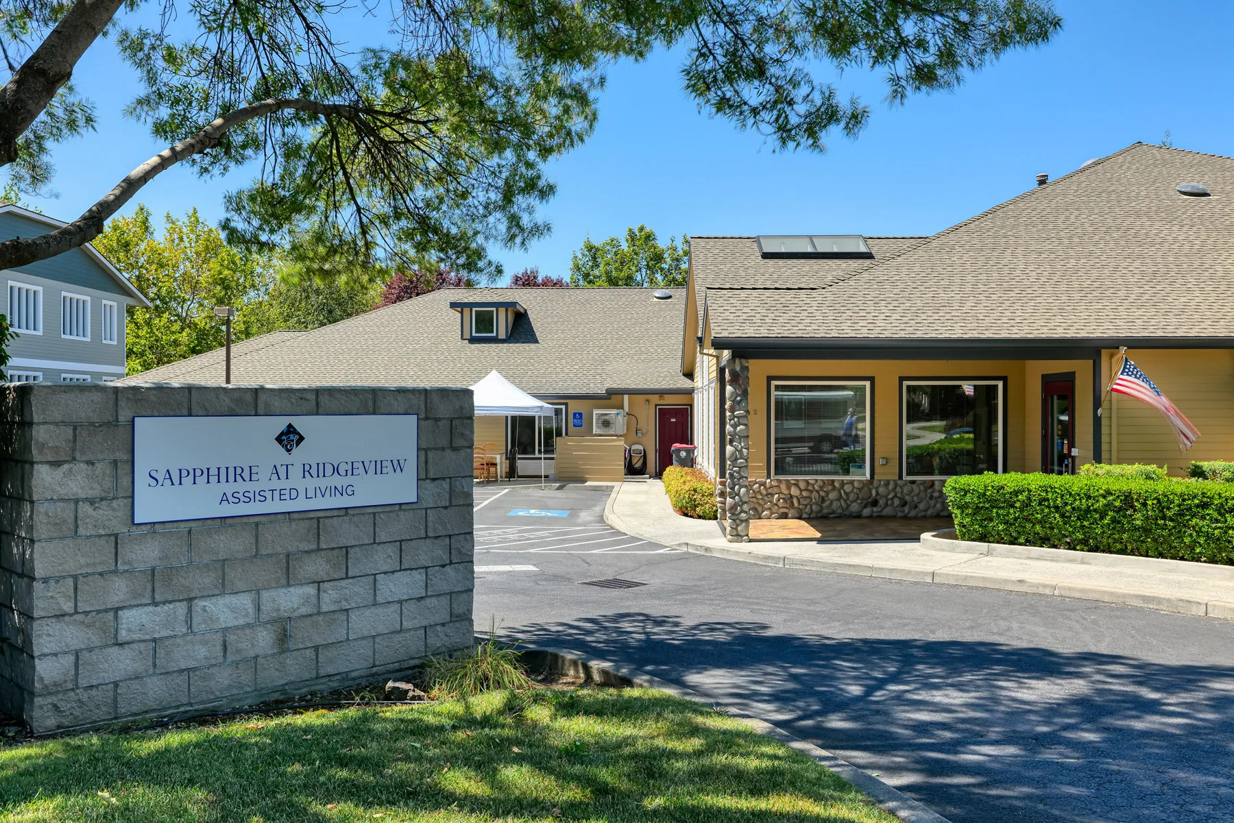 Exterior view of Sapphire at Ridgeview Assisted Living facility, featuring a sign, well-maintained landscaping, and an American flag